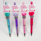 A collection of four beaded pens with 'Jesus Christ is king' printed on top, each with different color schemes and decorative elements.