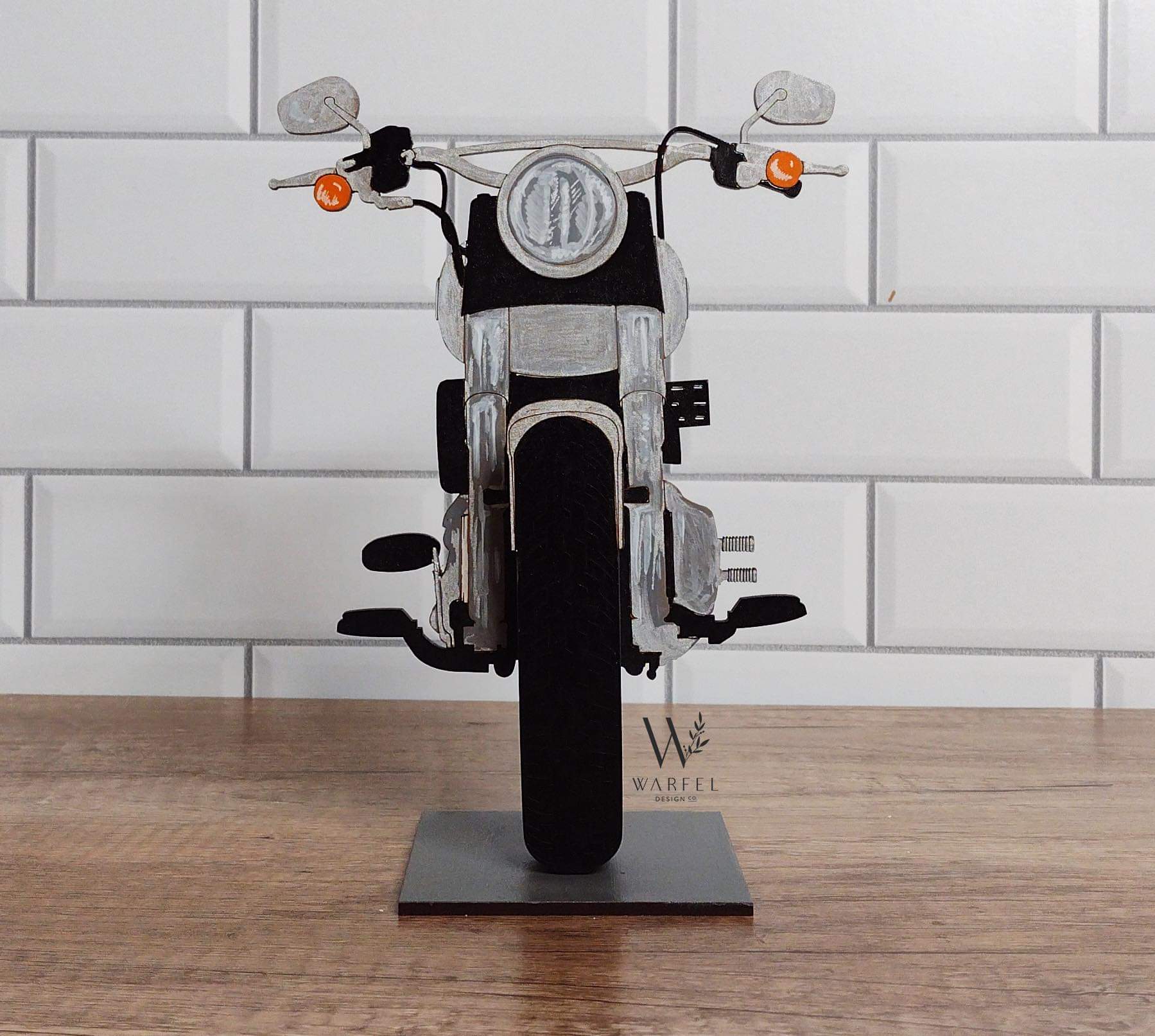 A motorcycle-shaped eyeglasses holder, with a black seat and silver metallic parts, displayed on a stand.