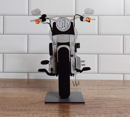 A motorcycle-shaped eyeglasses holder, with a black seat and silver metallic parts, displayed on a stand.
