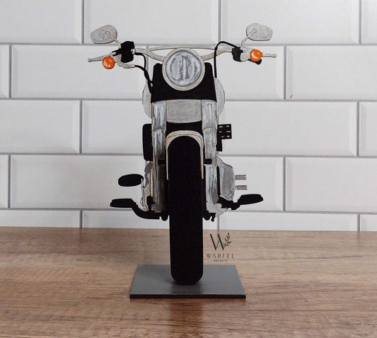 A motorcycle-shaped eyeglasses holder, with a black seat and silver metallic parts, displayed on a stand.