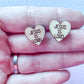 A pair of wooden stud earrings with the inscription 'JESUS IS LORD' on them, held between fingers.
